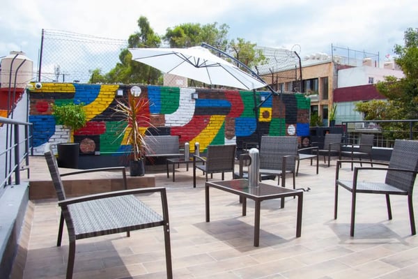 Nomadier rooftop terrace in Condesa with rattan chairs, a large umbrella, and a colourful painted mural on the wall